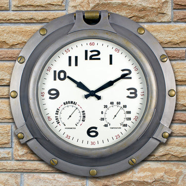 18” Silver Porthole Clock - faux brass screws and bolts around frame. Clock looks like a Porthole on a ship. shown hanging on a brick wall.