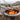 Hot dogs being cooked over an open flame in a metal container outdoors.