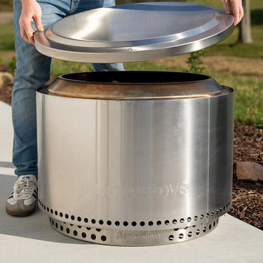 Stainless steel camp stove with lid held by a person outdoors