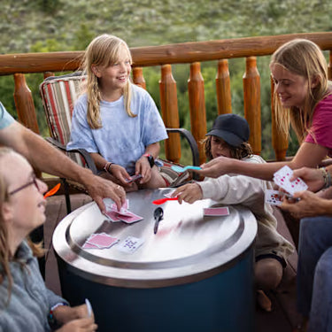 Group of people playing cards around a fire pit outdoors