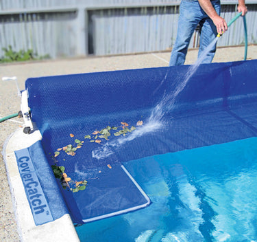 Cover Catch™ – Easy Leaf & Debris Removal for Solar Covers . pic shows man using water hose to hose leaves off cover and into the cover catch.