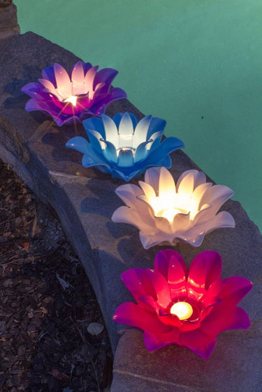 4 Lotus lights in blue white pink and purple sitting beside pool and lit up with  tea light candles