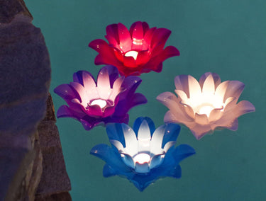 4 Lotus lights in blue white pink and purple sitting in pool lit up with tea light candles