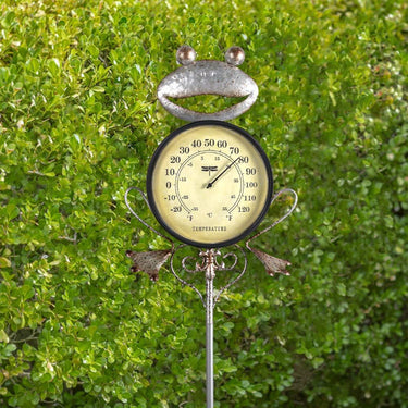Frog Thermometer Garden Stake - Silver metal frog with round thermometer as his body. attached to a garden stake with adjustable height. shown how fun it is outside next to some greenery.