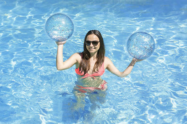 16" Silver Glitter Play Ball - 2 pack. Ball is transparent with different color/silver glitter. Shown with a young lady holding them both up while standing in pool water.