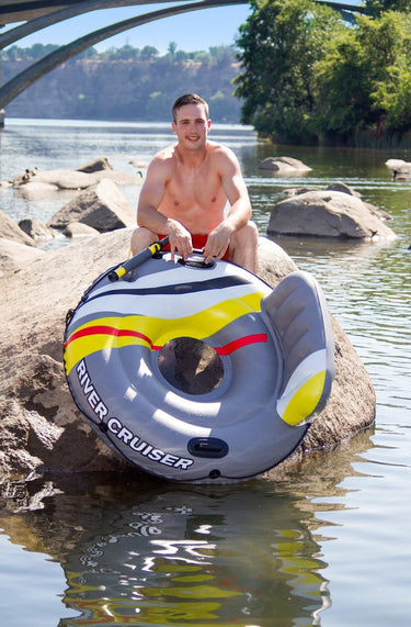 47” DLX River Cruiser Lounge With water launcher. Grey with yellow, red, white and black strip design. 2 handles to hang onto and a back rest. Man sitting on a rock in the river holding it for scale.