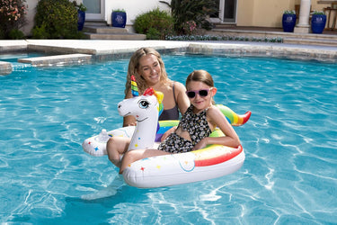 Unicorn Rainbow Rider for children. shown with young girl floating in it with her mom standing the in pool next to her.