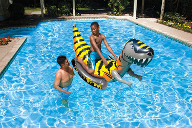 T-Rex Rider - Large Dinosaur Pool Float for adults or children over 8 years old.  Shown with a teenage boy floating in the water with adult man standing next to him.