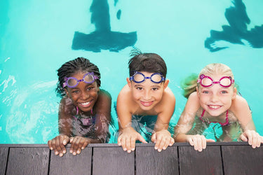 3 children holding onto side of pool each one wearing a pair of swim goggles.