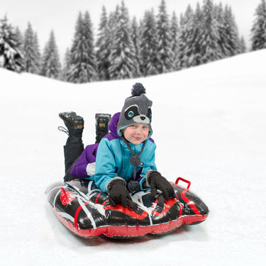 Snow Trax - heavy duty inflatable sled. Black with white design and red handles to hold on with. Shown with young boy on it in the snow.