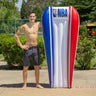  74.5” L x 44” W (deflated) NBA Poolmaster mattress float. blue striped on one side red striped on the other side and otherwise white with the NBA Logo on the pillow. Man standing next to it for scale.