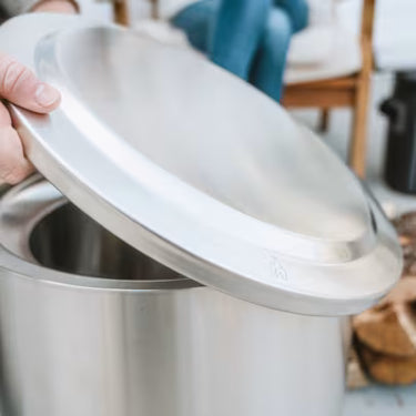 Person holding a large metal pot with a lid indoors