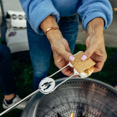 Person roasting a marshmallow over a campfire with a metal roasting stick.