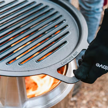 Person using a portable grill with visible flames, wearing a glove.