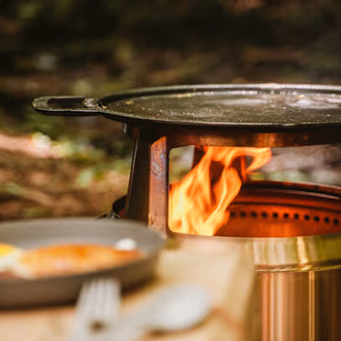 Campfire with a metal pan on top, surrounded by nature