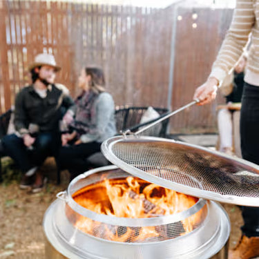 People sitting around a fire pit with a person using tongs