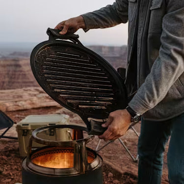 Person setting up a portable stove outdoors with a scenic background