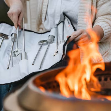 Person using grill tools over a fire pit with flames