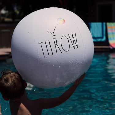 Child holding Jumbo White Beach Ball with Throw in text, in the pool.
