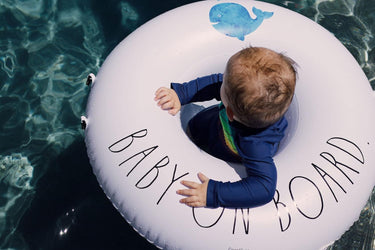 White and Blue Baby Ring float showing without canopy with baby riding in water. Text Baby on Board and graphic of Blue Whale
