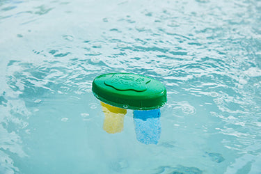 Green and yellow pool sanitizing system floating on water