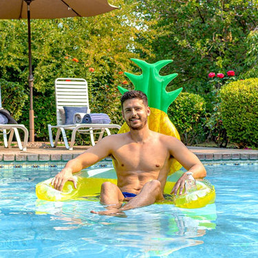 Man sitting on a pineapple-shaped inflatable pool float in a swimming pool.