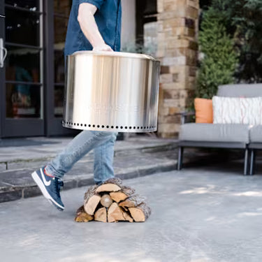 Person carrying a metal stove with firewood outside a house
