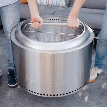 Two people holding a large stainless steel fire pit