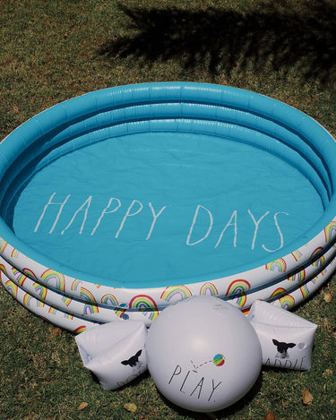 Child inflatable pool with rainbows and Happy Days text in grass